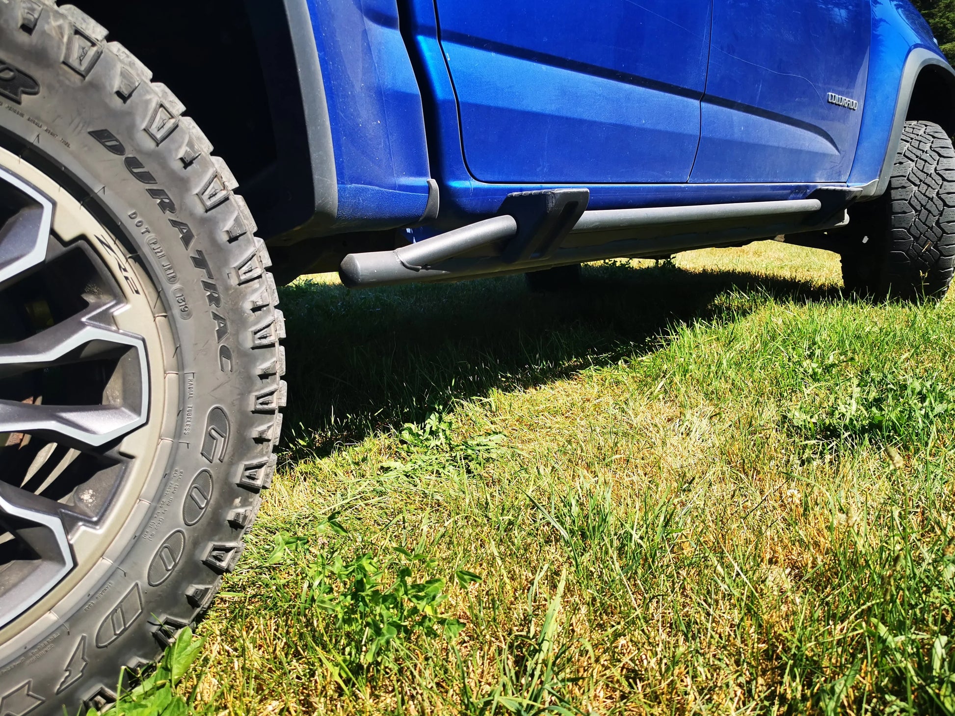 Blue off-road truck with Goodyear Duratrac tire and snap-on sidestep on grass