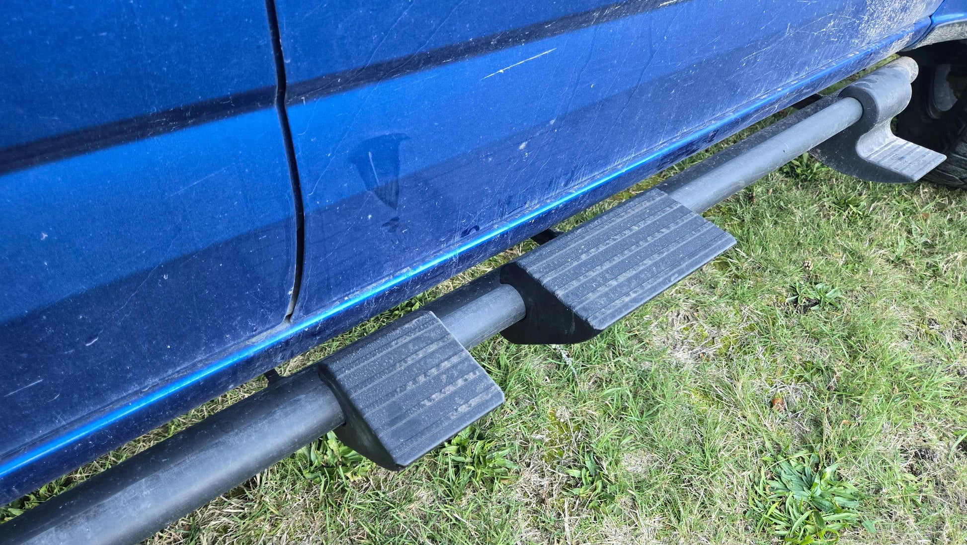 Snap-on sidesteps installed on a blue truck, shown parked on grass.